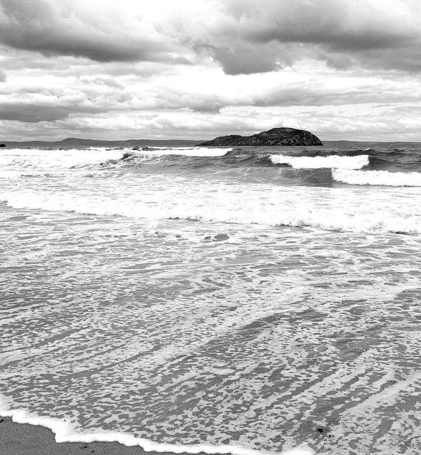 Black and white monochrome picture of waves crashing on a beach with a small rocky outcrop in the centre of the frame. We don't really consider the ocean to be alive but it is still teaming with life. Is that like soil?